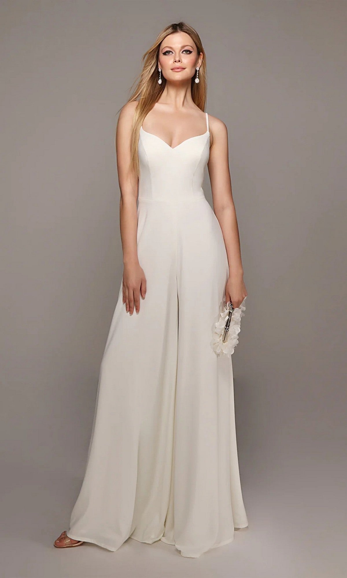 A woman wearing the Alyce 70022 Long White Jumpsuit, featuring wide-leg pants and a sweetheart neckline, holds a floral-detailed purse against a plain background.